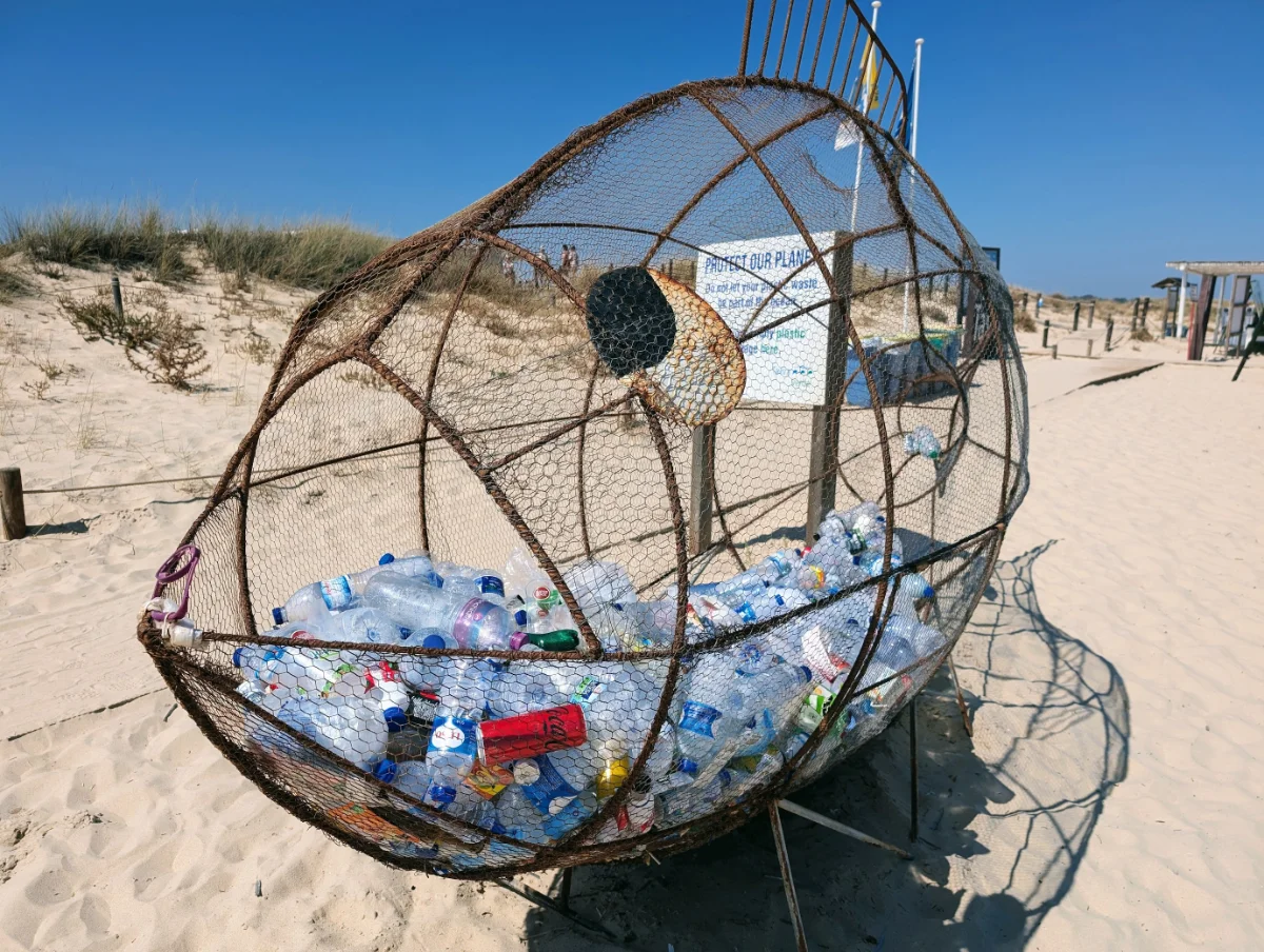 Bild eines Müllfisches aus Stahl am Strand mit leeren Plastikflaschen