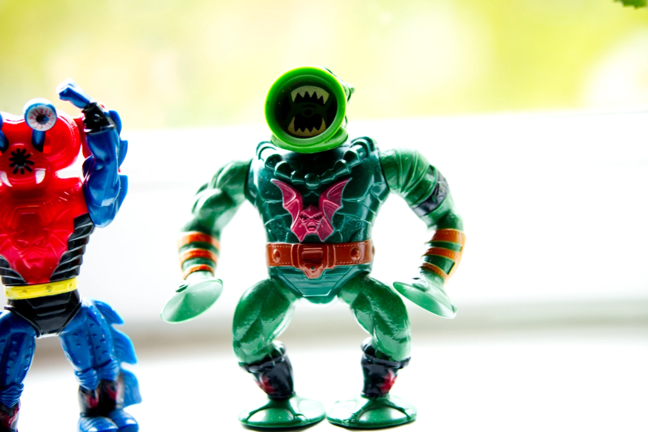 wei Vintage-Actionfiguren aus der Masters of the Universe-Reihe auf einer hellen Fensterbank. Im Fokus steht die grüne Figur Leech mit großen Saugnäpfen als Mund, Händen und Füßen sowie dem roten Horde-Emblem auf der Brust. Links daneben ist die blau-rote Figur Mantenna mit großen Glubschaugen angeschnitten zu sehen. Der Hintergrund ist hell und unscharf.
